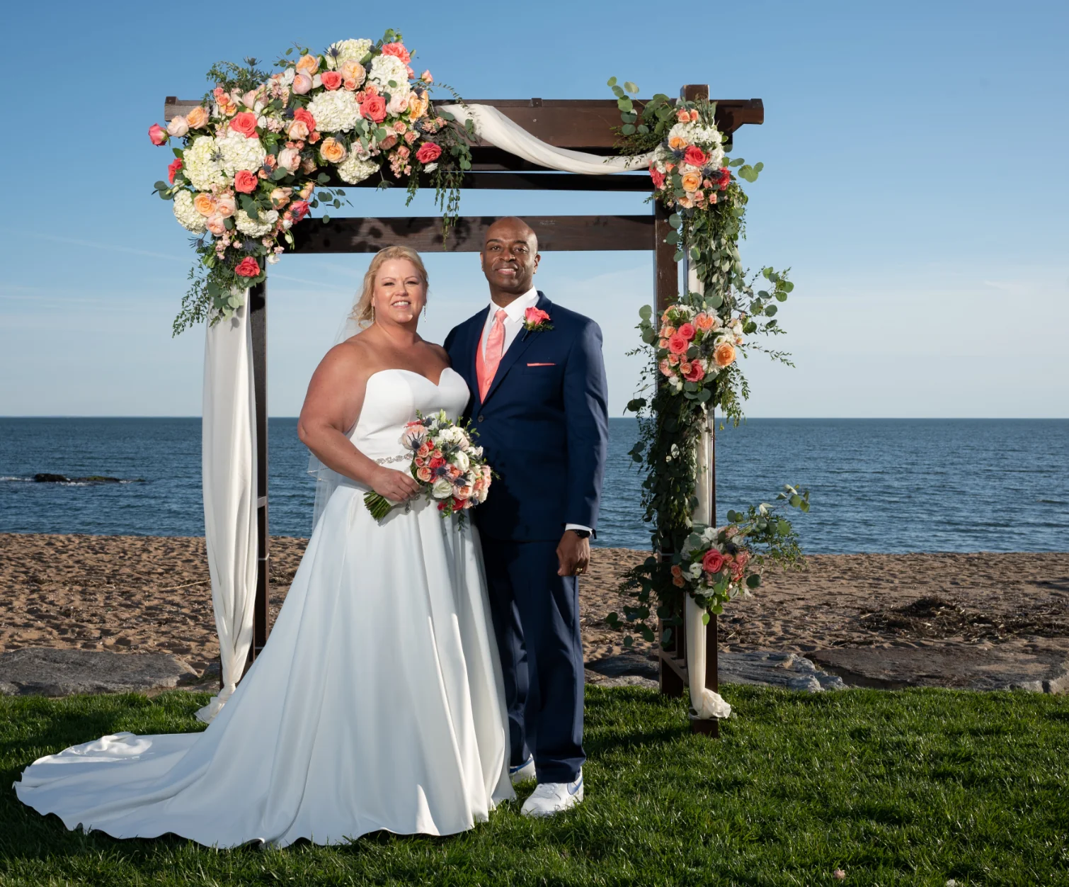 Married couple posing in front of an arch near the water