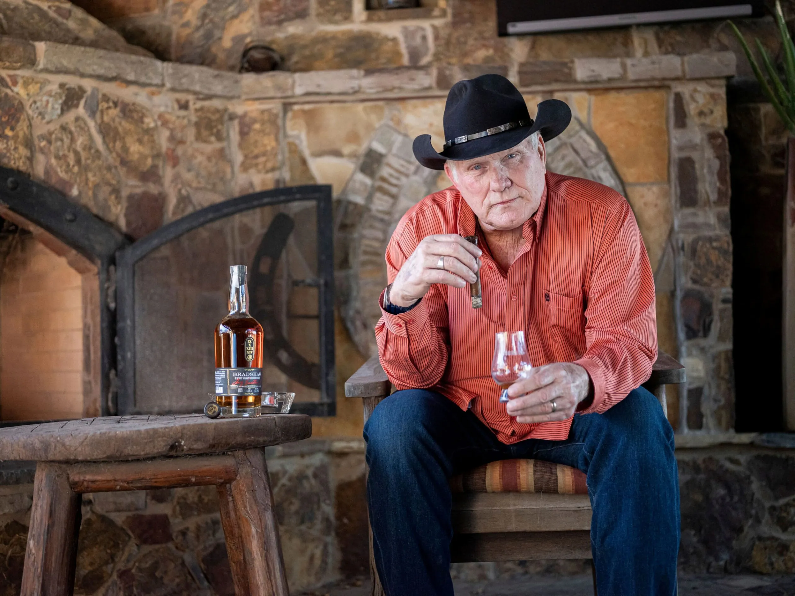 Terry Bradshaw sitting by fireplace with bradshaw bourbon